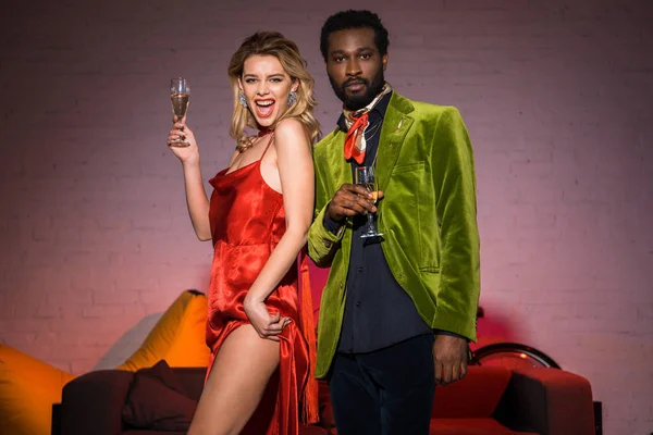 Low angle view of excited blonde girl holding champagne glass near african american man — Stock Photo