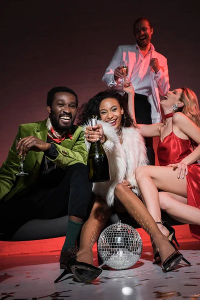 Low angle view of african american man holding champagne glass while sitting with multicultural friends — Stock Photo