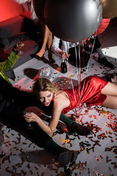 Vista aerea della ragazza felice che tiene i palloncini mentre giace sul pavimento vicino agli amici — Foto stock