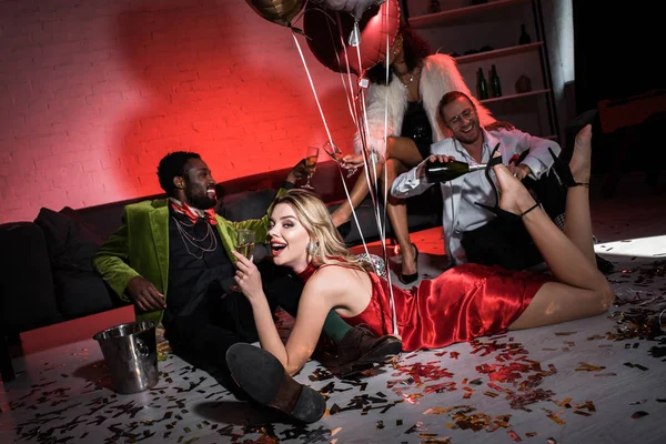 Happy girl holding balloons while lying on floor near multicultural friends — Stock Photo