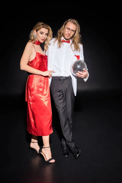 Attractive woman in red dress standing near man in glasses with disco ball on black — Stock Photo