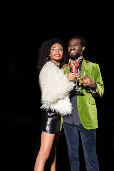 Cheerful african american girl and handsome african american man holding champagne glasses isolated on black — Stock Photo