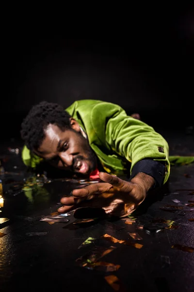 Selective focus of drunk african american man lying on floor with shiny confetti on black — Stock Photo