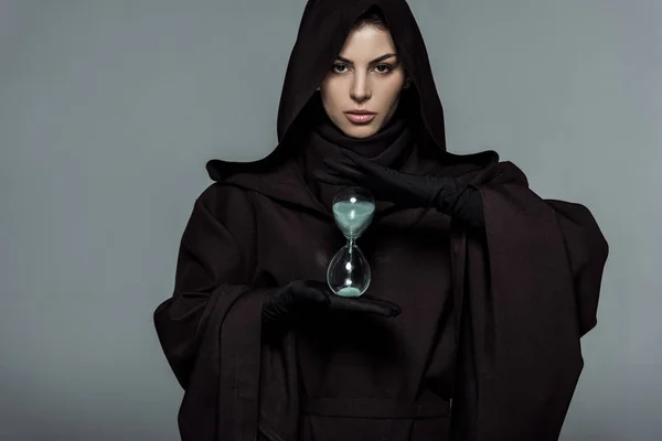 Vista frontal de la mujer en traje de la muerte sosteniendo reloj de arena aislado en gris - foto de stock