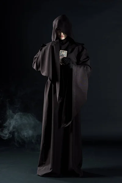 KYIV, UCRAINA - 18 APRILE 2019: veduta a figura intera di donna in costume da morte con in mano tarocchi su nero con fumo — Foto stock