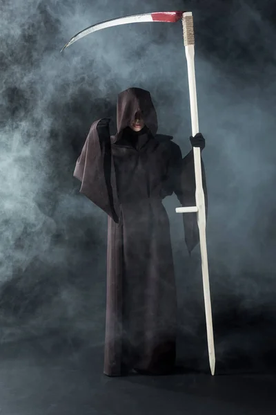 Full length view of woman in death costume holding scythe on black with smoke — Stock Photo