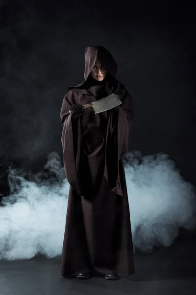 Full length view of woman in death costume holding cleaver in smoke on black — Stock Photo