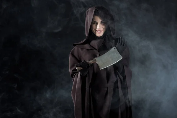 Woman in death costume holding cleaver in smoke on black — Stock Photo