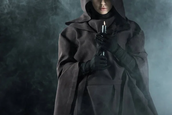 Vista parcial de la mujer en traje de la muerte sosteniendo vela en el humo en negro - foto de stock
