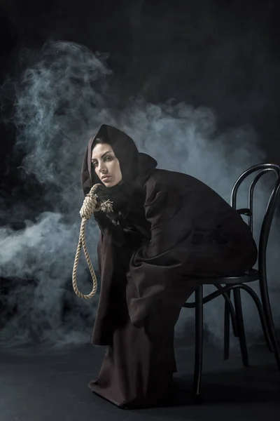 Жінка в костюмі смерті сидить на стільці і тримає висячі нори на чорному — стокове фото