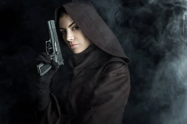 Mujer en traje de la muerte sosteniendo la pistola y mirando a la cámara en negro - foto de stock