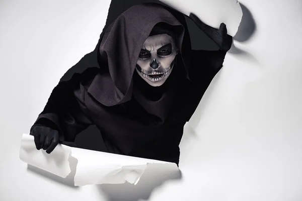 Женщина в костюме смерти вылезает из дыры в бумаге — стоковое фото