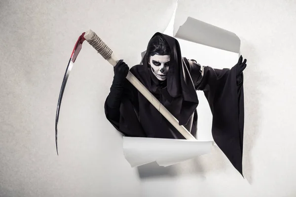 Woman in death costume holding scythe and getting out of hole in paper — Stock Photo