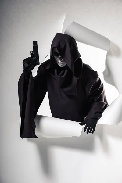 Жінка в костюмі смерті тримає пістолет і виходить з отвору в папері — стокове фото
