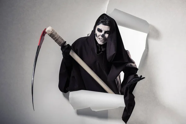 Woman in death costume holding scythe and getting out of hole in paper — Stock Photo