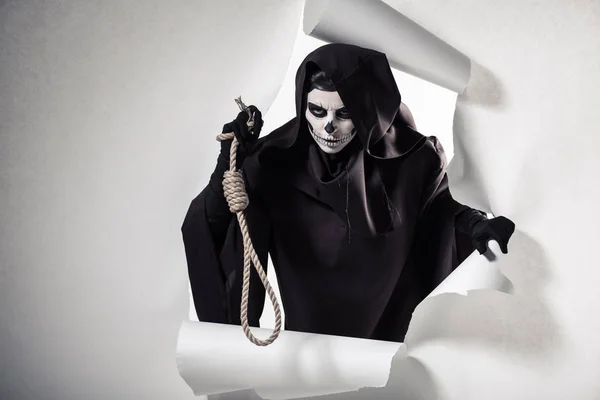 Frau im Todeskostüm hält Schlinge in der Hand und steigt aus Loch in Papier — Stockfoto