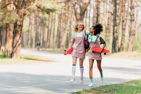 Volle Länge Ansicht der lachenden multiethnischen Freunde mit Penny-Boards springen auf der Straße — Stockfoto