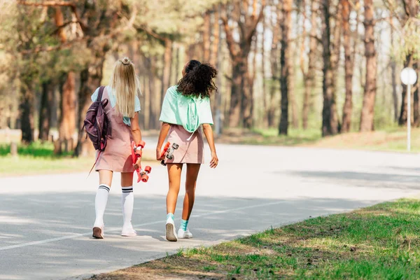 Visão traseira de dois amigos multiculturais com tábuas penny andando na estrada — Fotografia de Stock