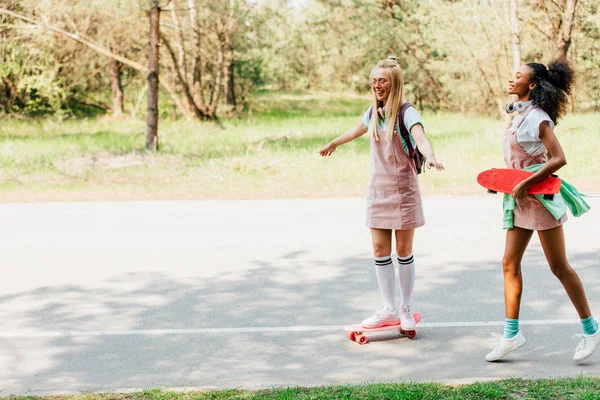 Vista completa di due amici multiculturali skateboard su strada con sorriso — Foto stock