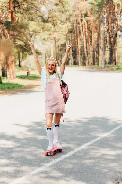 Piena vista lunghezza di eccitata ragazza bionda skateboard e ascoltare musica in cuffia — Foto stock