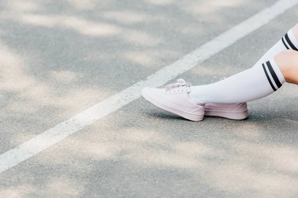 Частичный вид девушки в белых носках на коленях, сидящей на дороге — стоковое фото