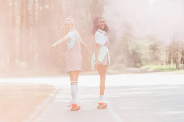Full length view of two girls skateboarding on penny boards in smoke on road — Stock Photo