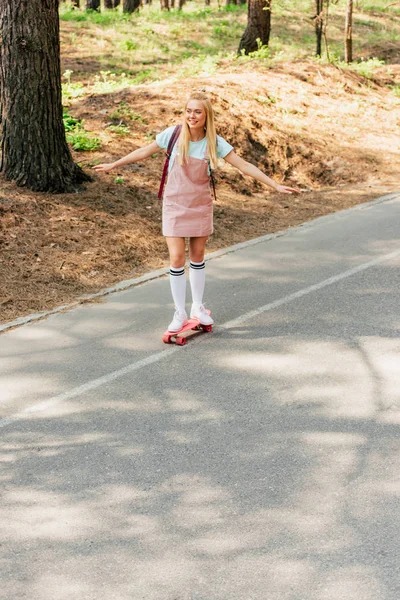 Vista completa de la chica rubia en calcetines de rodilla skateboarding en la carretera - foto de stock