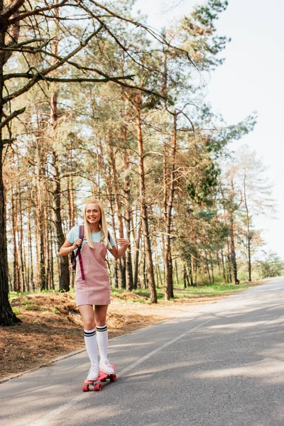 Visão de comprimento total da menina loira em meias de joelho skate na estrada — Fotografia de Stock