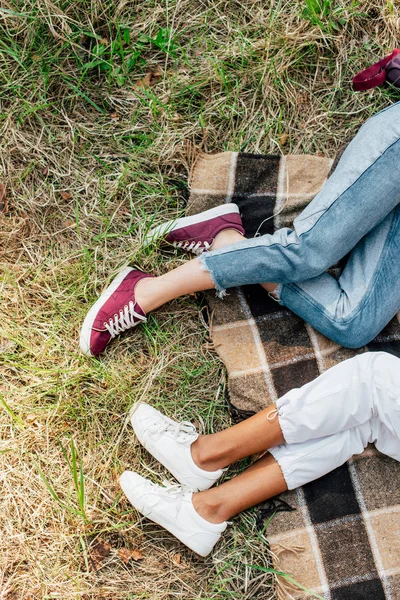 Top view of two multiethnic friends lying on plaid blanket on ground — Stock Photo