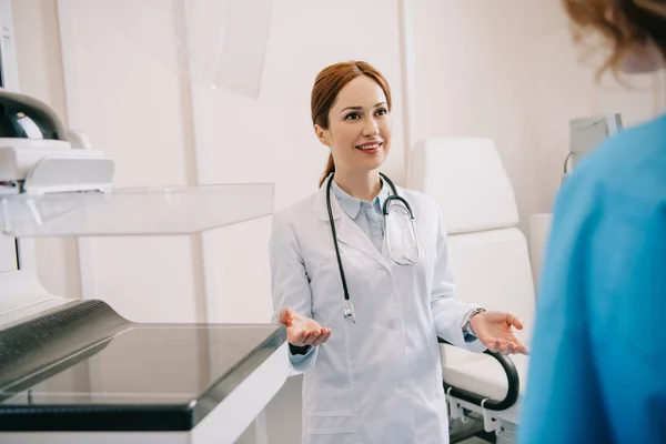 Foco seletivo de belo médico sorridente no casaco branco acolhedor paciente no hospital — Fotografia de Stock