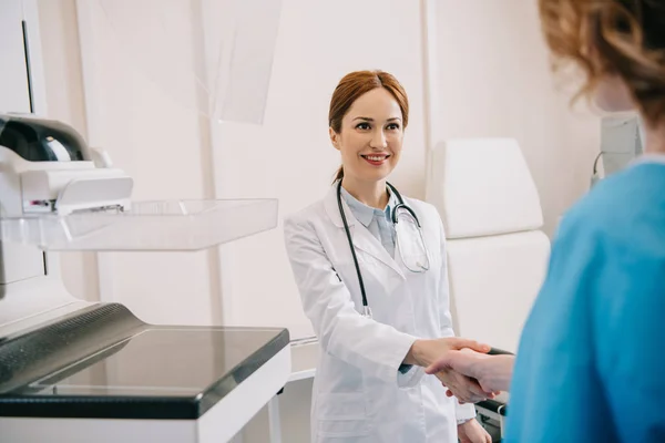 Enfoque selectivo del radiólogo sonriente estrechando la mano con el paciente en el hospital - foto de stock