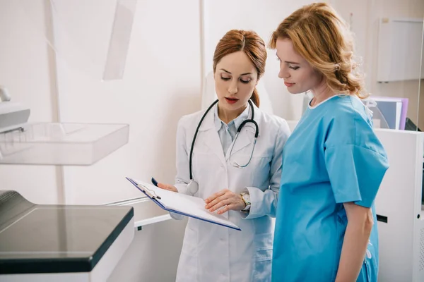 Attractive young doctor and patient looking at diagnosis on clipboard — Stock Photo