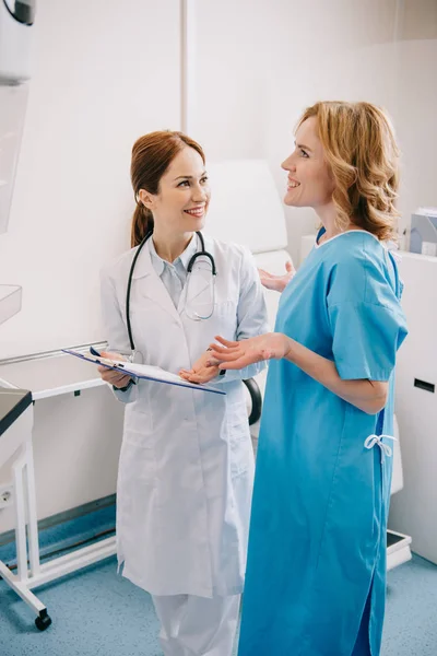 Улыбающийся доктор держит планшет, стоя рядом с счастливым пациентом — стоковое фото