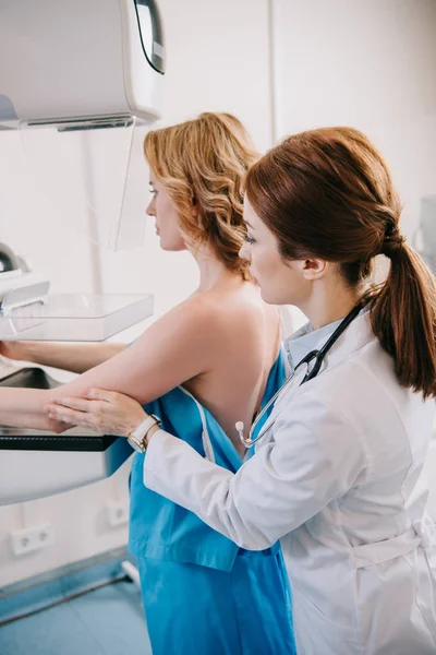 Уважний радіолог готує жінку до тесту мамографії на рентгенівській машині — стокове фото
