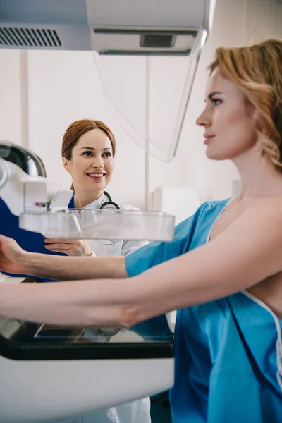 Selective focus of smiling doctor standing near patient during mammography test on x-ray machine — Stock Photo