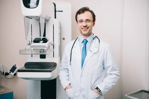 Schöner Radiologe, der neben dem Röntgengerät steht und in die Kamera schaut — Stockfoto