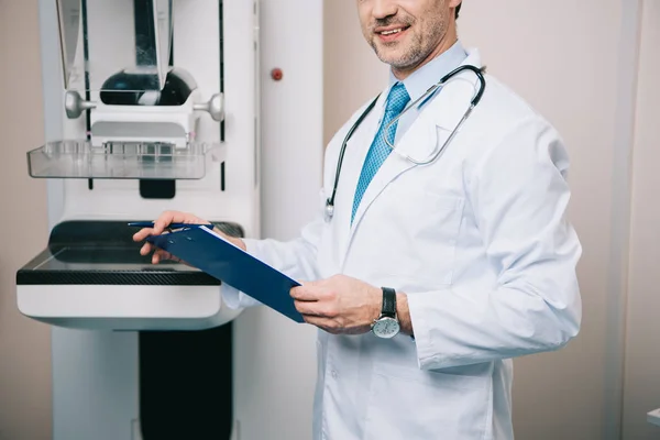 Partial view of doctor holding clipboard while standing at x-ray machine — Stock Photo