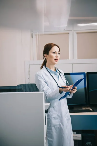 Selective focus of pretty young doctor gesturing while holding clipboard — Stock Photo