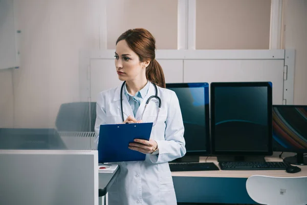 Selective focus of attentive doctor writing on clipboard and looking away — Stock Photo