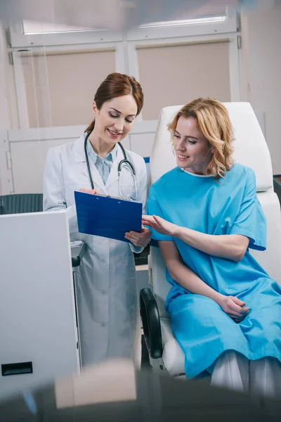 Selective focus of young doctor and beautiful woman looking at clipboard with diagnosis — Stock Photo