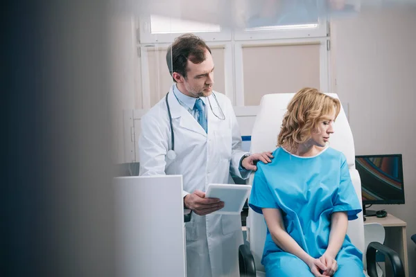 Foyer sélectif du médecin tenant comprimé numérique et toucher l'épaule de la femme bouleversée — Photo de stock