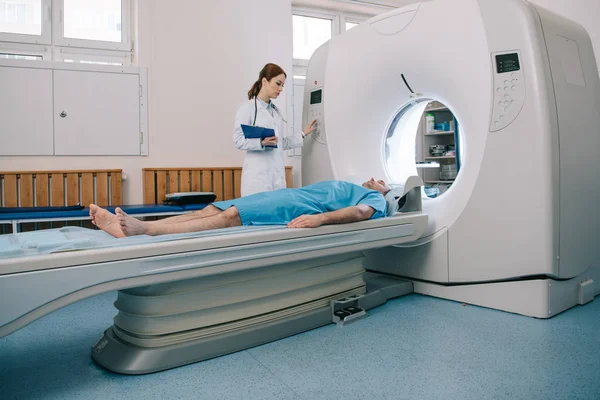 Young radiographer operating ct scanner while preparing patient for tomography — Stock Photo