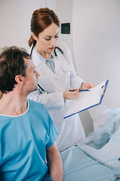 Vista recortada del médico atento que muestra portapapeles con diagnóstico al paciente - foto de stock