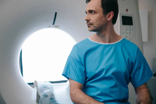 Thoughtful patient sitting on ct scanner bed in hospital and looking away — Stock Photo