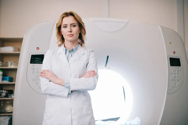 Attractive confident radiologist standing near mri machine with crossed arms and looking at camera — Stock Photo