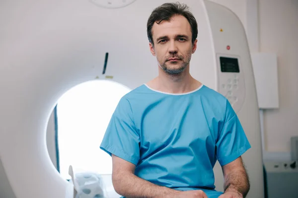 Thoughtful man sitting on ct scanner bed and looking at camera — Stock Photo