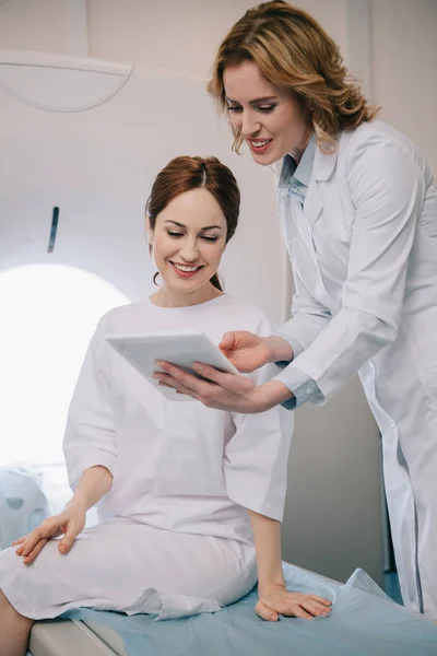 Cheerful radiologist showing digital tablet with x-ray diagnosis to happy patient — Stock Photo