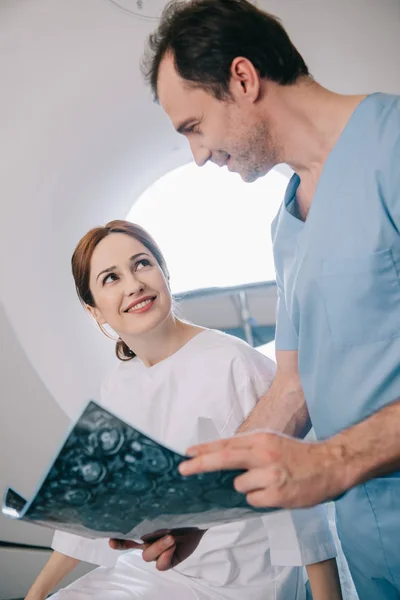 Médico sorrindo mostrando tablet digital com diagnóstico de raio-x para paciente feliz — Fotografia de Stock