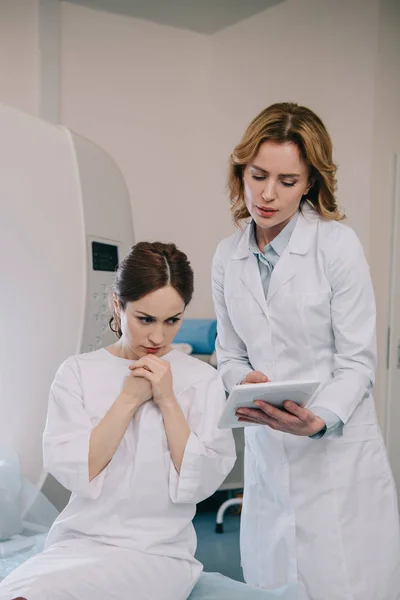 Schöne Ärztin zeigt besorgter Frau digitales Tablet mit Röntgendiagnose — Stockfoto