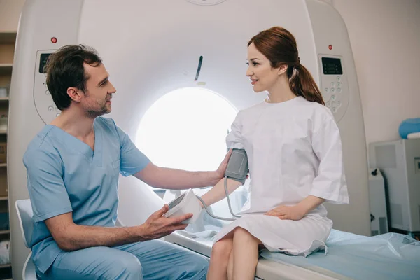 Handsome doctor measuring patients blood pressure with tonometer while sitting at mri scanner — Stock Photo